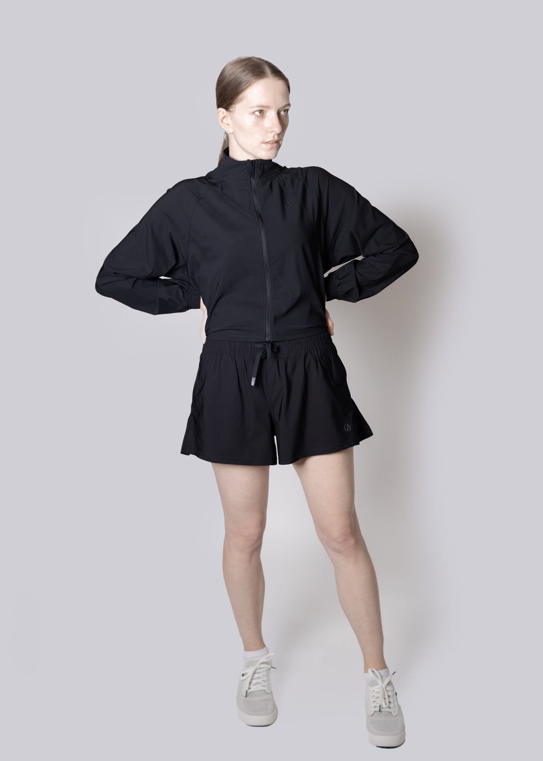 A girl wearing a black outfit with a jacket and shorts on a plain background
