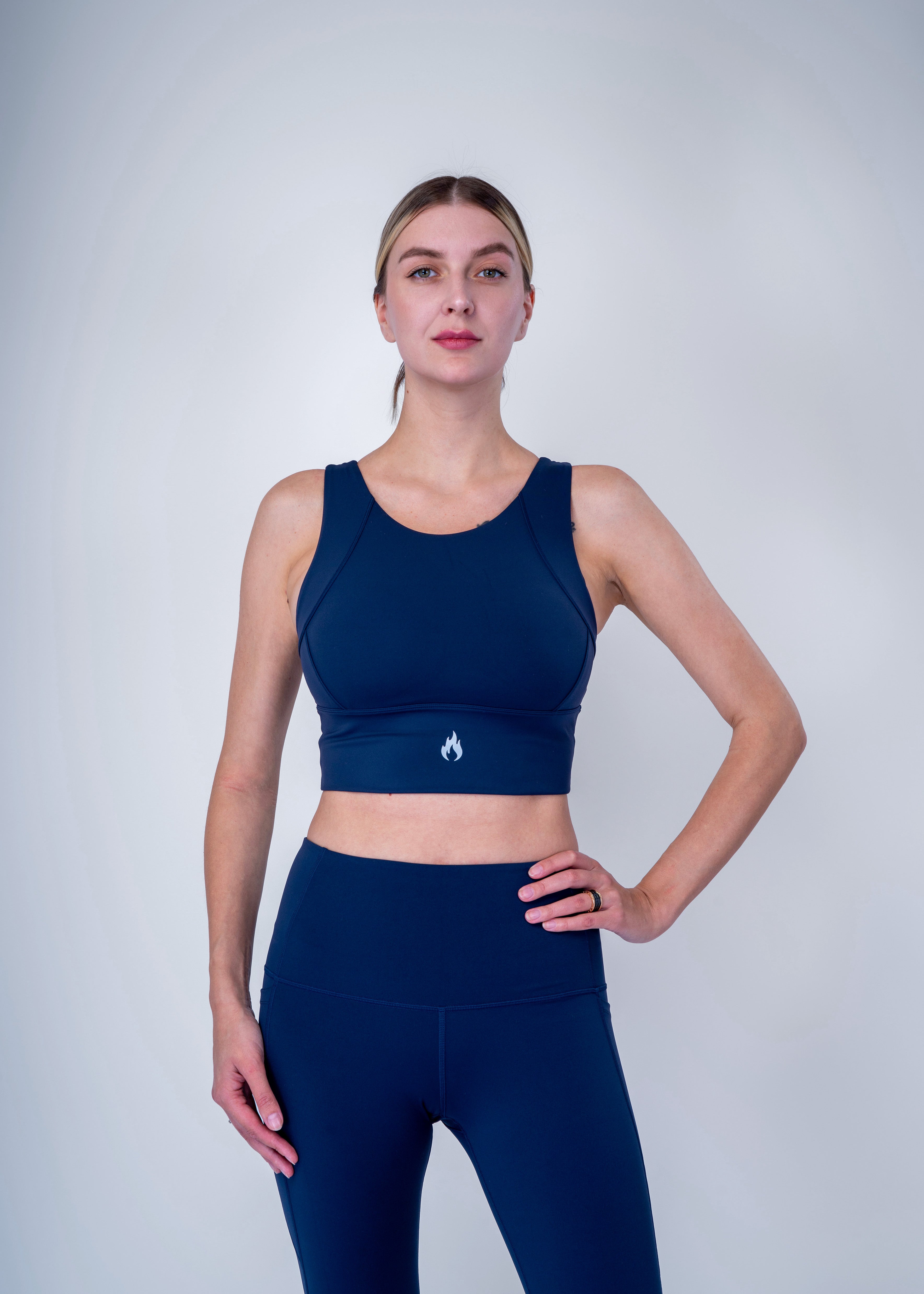 Woman wearing a navy blue sports bra and leggings with a white Spofire logo on a light gray background 
