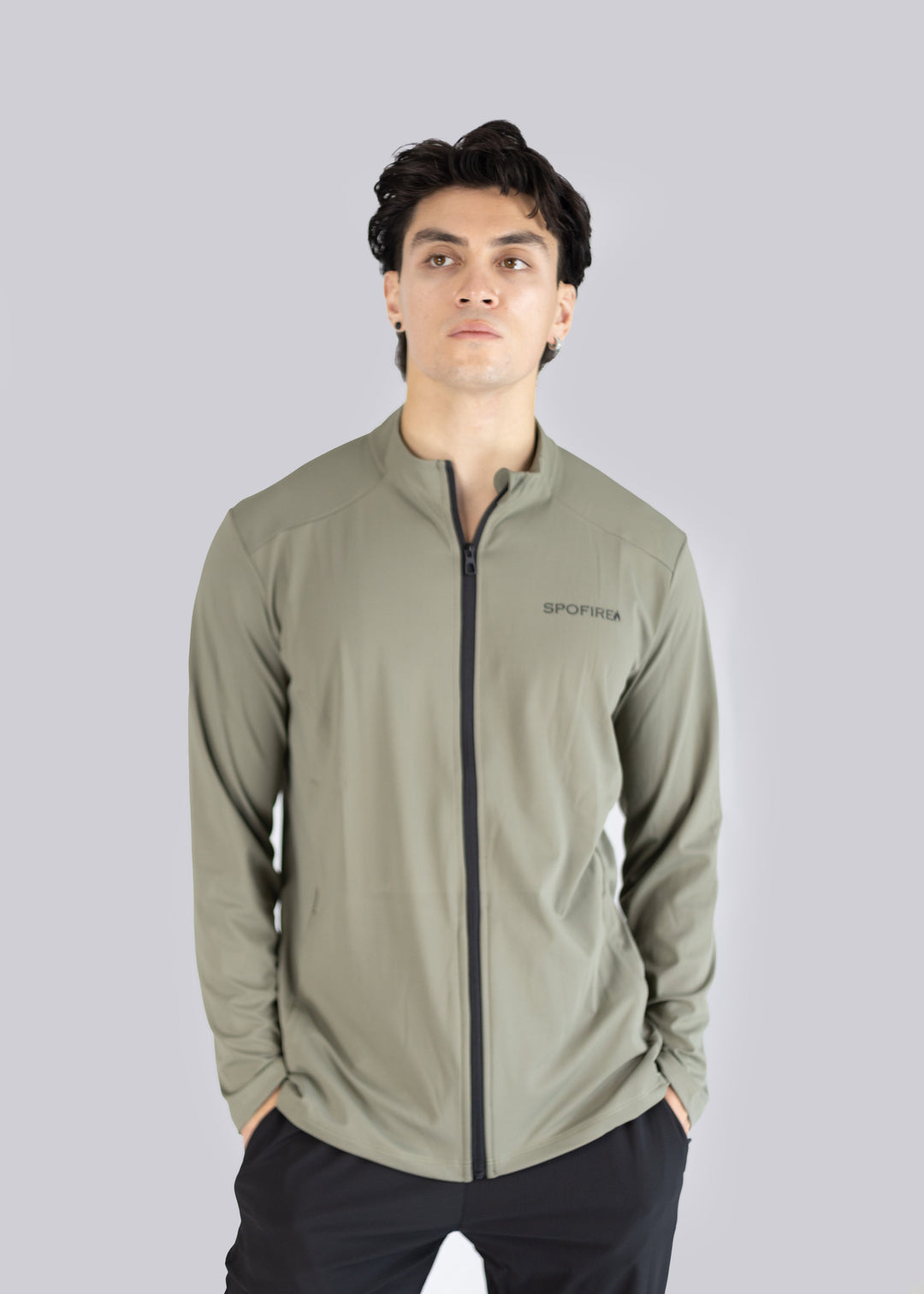 A man wearing an olive  jacket with a brand logo on a gray background