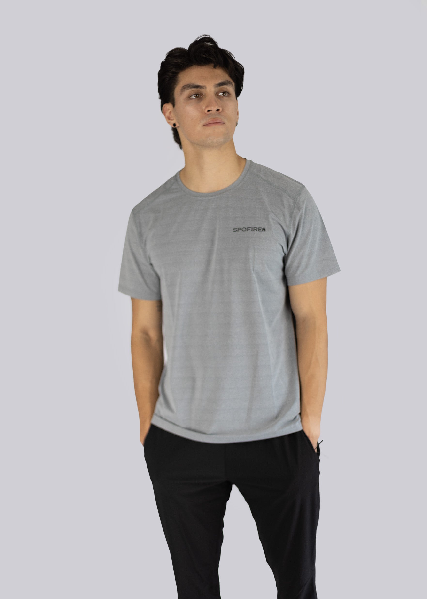 A man wearing a gray t-shirt with the Spofire logo on a light gray background, hands inside his pants pockets