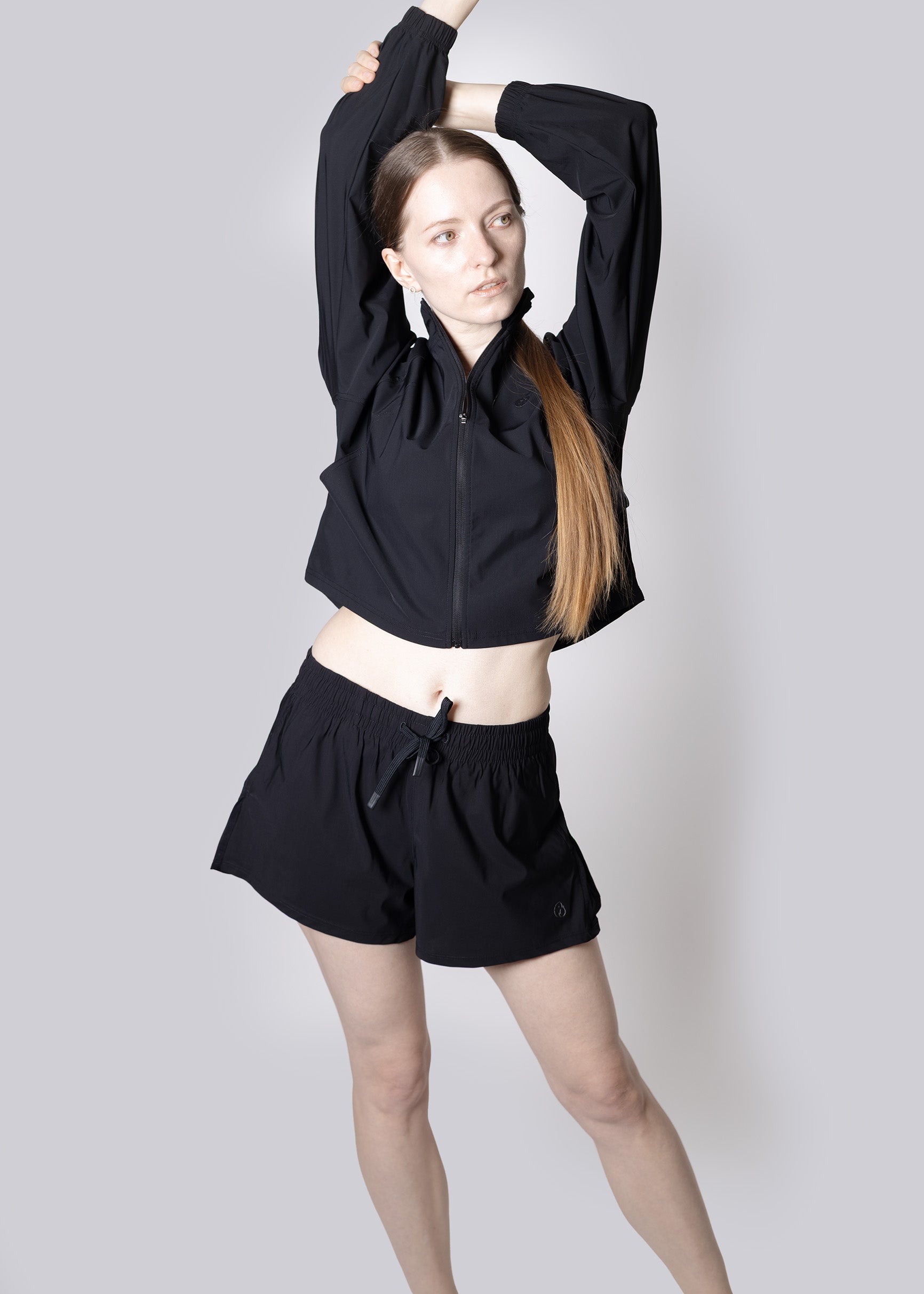 A woman wearing a black outfit with a jacket and shorts on a plain background