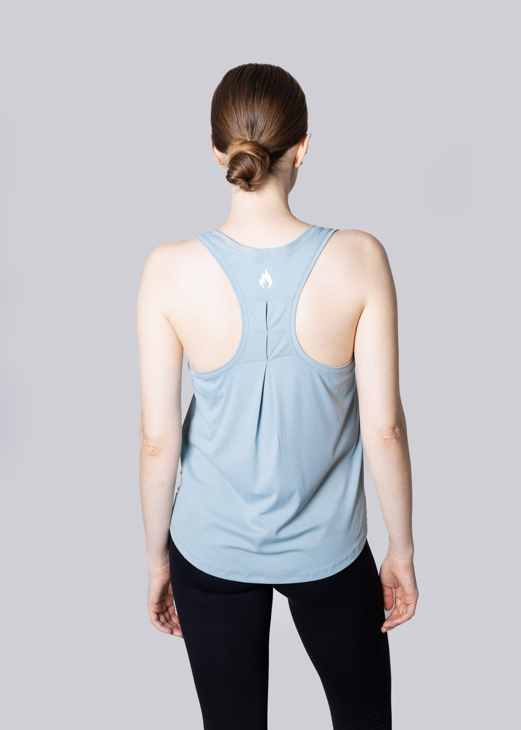A girl wearing a light blue tank top with a subtle pattern on a plain background