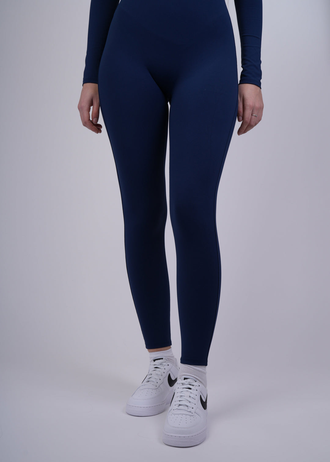 A model wearing a navy blue jumpsuit and white sneakers on a light gray background