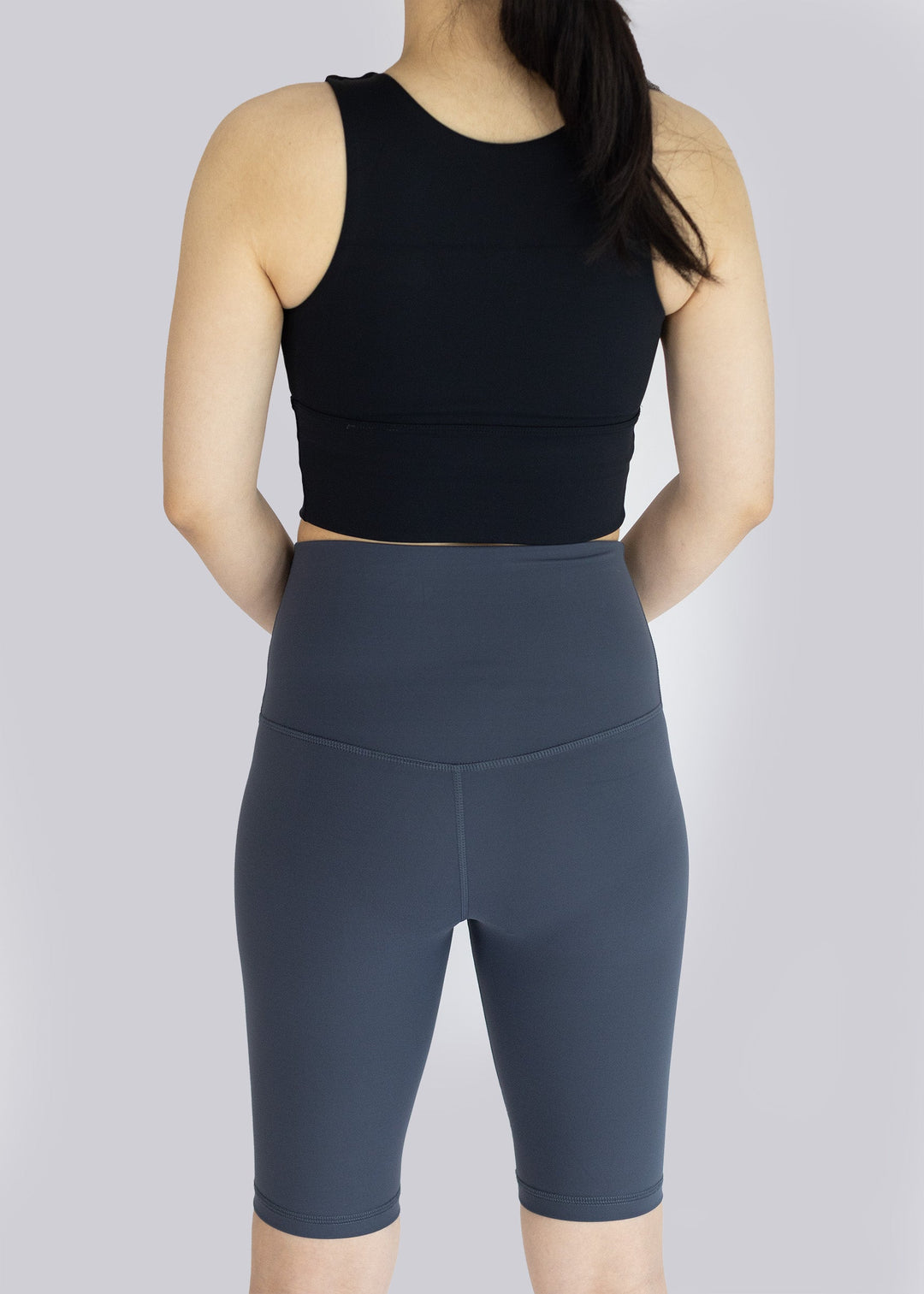 A woman  wearing a black sleeveless top and dark gray shorts on a light gray background
