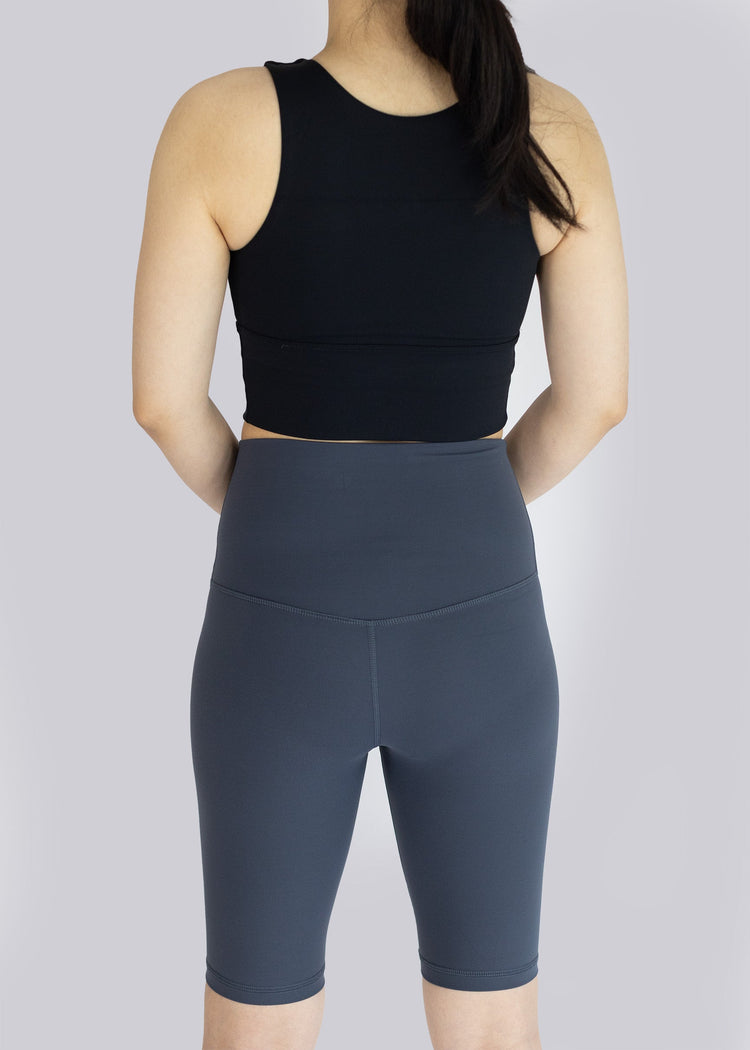 A woman  wearing a black sleeveless top and dark gray shorts on a light gray background