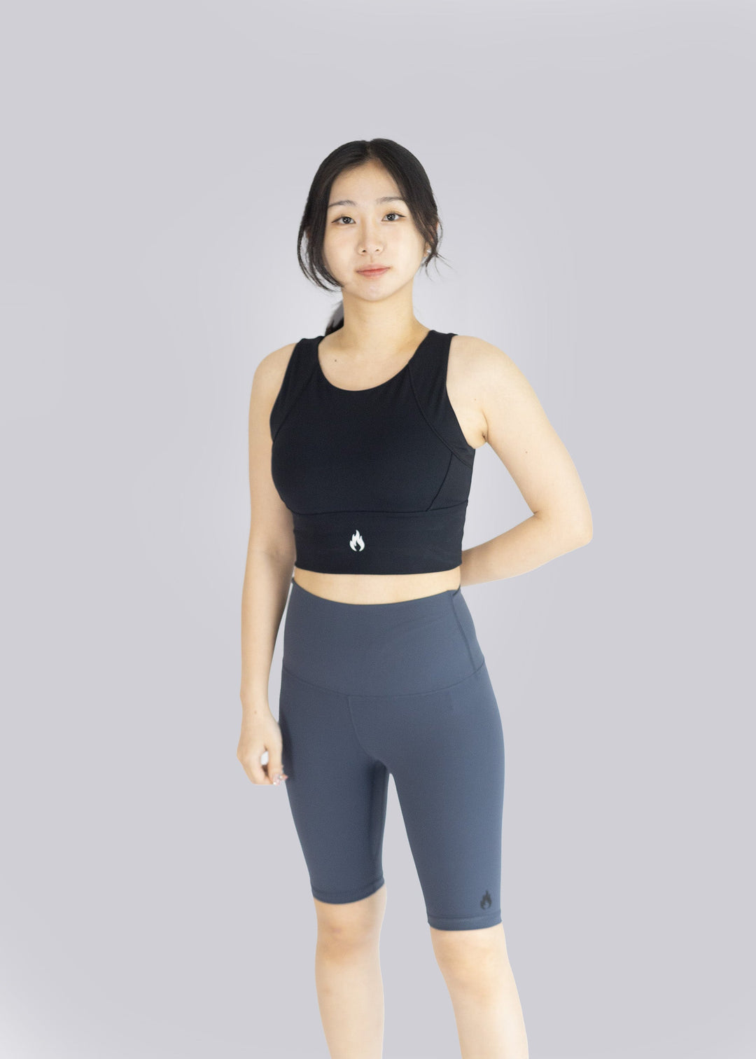 A woman wearing a black sports bra and Blue shorts on a plain background