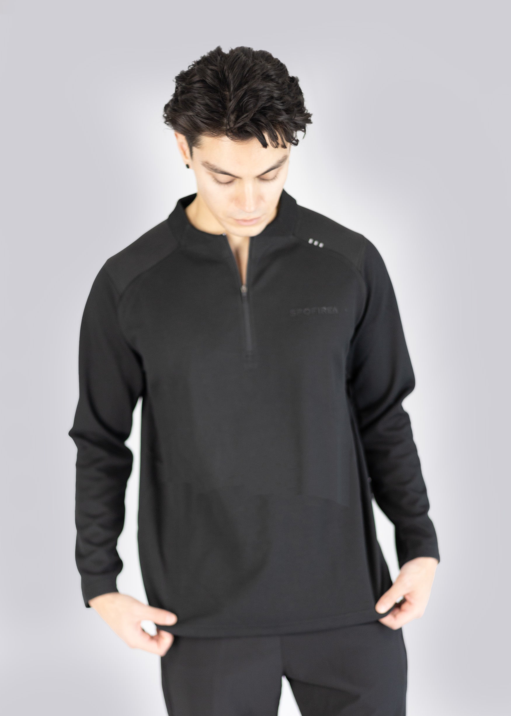 Man wearing a black long-sleeve athletic sweater on a gray background